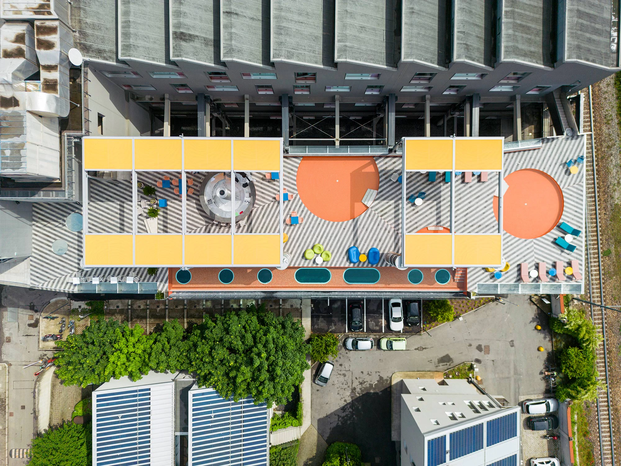 Vista dall'alto della terrazza Vertigo Pool Milano con pavimentazione geometrica, arredi colorati e una imponente struttura metallica per ombreggiamento realizzata da Fratelli Gelmini.
