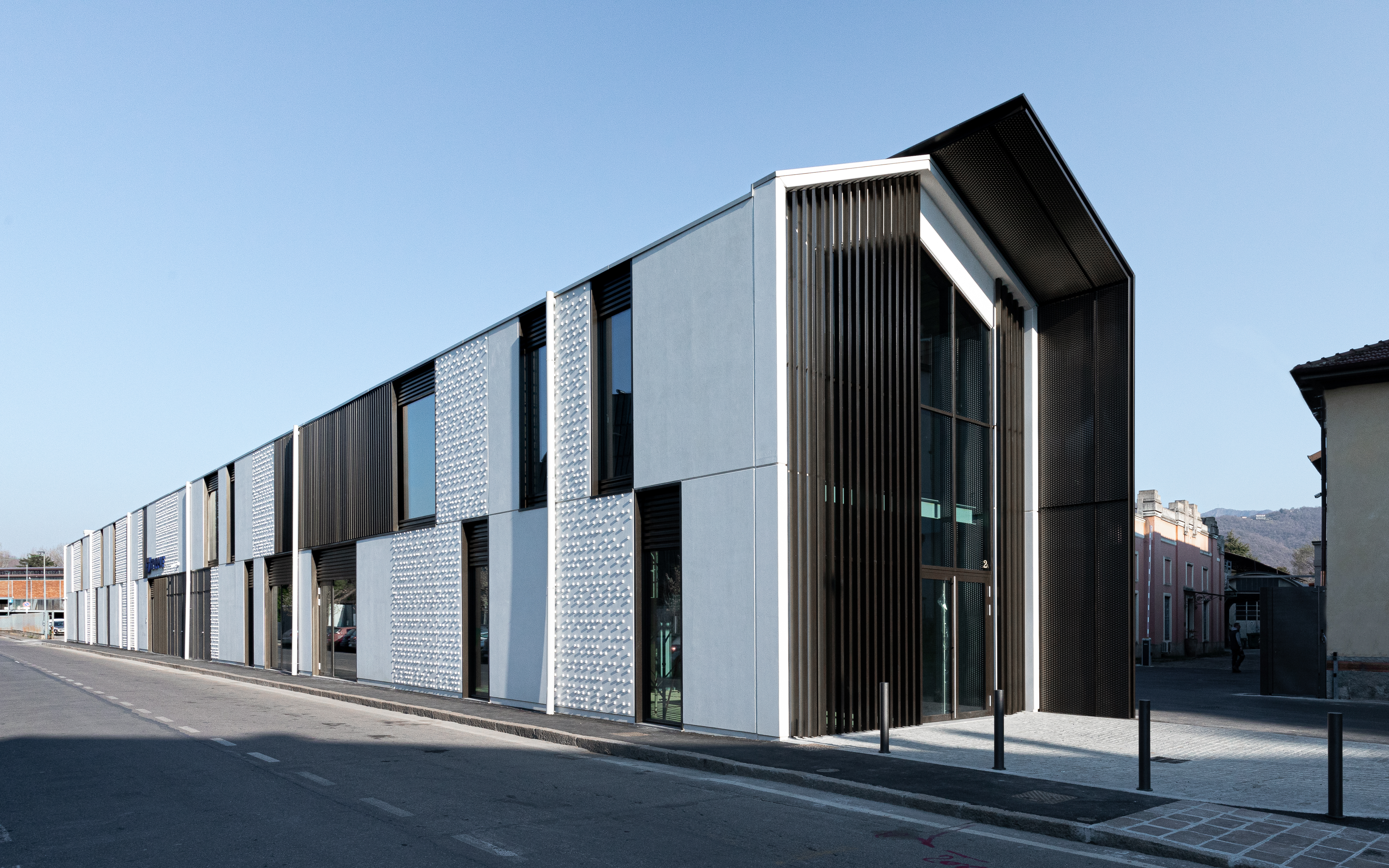 Facciata industriale con brise-soleil metallici e imbotte strutturale nera, progetto Trafilerie Mazzoleni realizzato da Fratelli Gelmini.